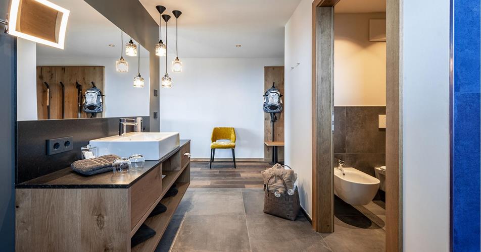 Bagno moderno con grande specchio, lampade sospese, mobili in legno e WC separato con bidet.