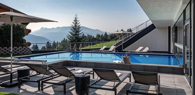 Moderner Außenpool mit stilvollen Liegen, Sonnenschirmen und Panoramablick auf bewaldete Berge und Täler in der Morgensonne.