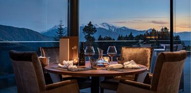 Tavolo apparecchiato con vino e candele, vista panoramica sulle montagne al tramonto.