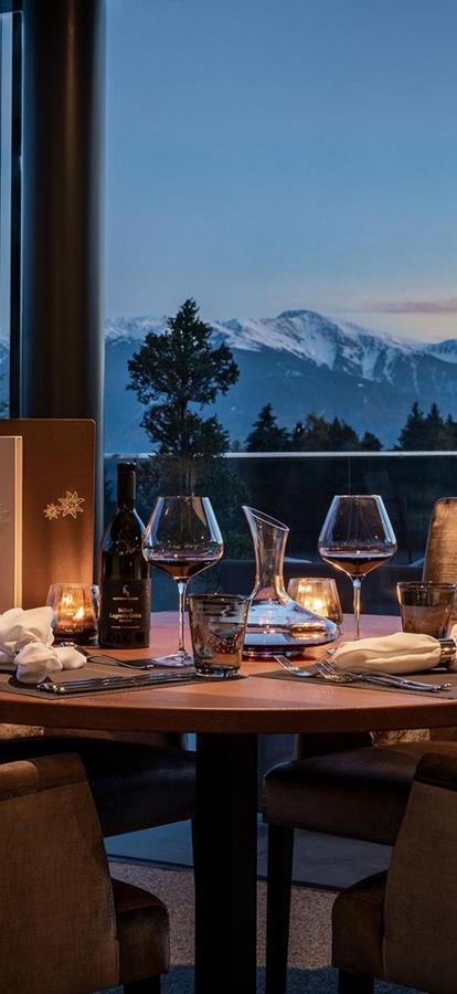 Atmospheric dinner table with wine and candlelight, overlooking mountain panorama at sunset.