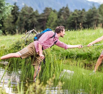 Two hikers are crossing over a stream