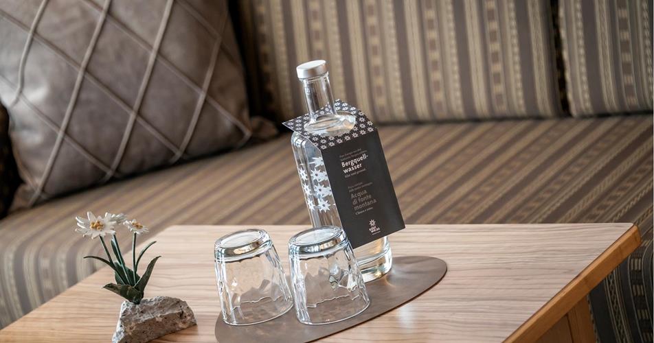 Flasche mit Bergquellwasser und zwei Gläsern auf einem Holztisch