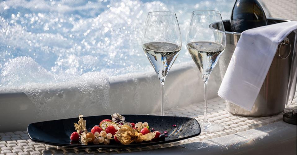 Outdoor whirlpool with bubbling water, two glasses of sparkling wine, fruit plate, and champagne cooler.