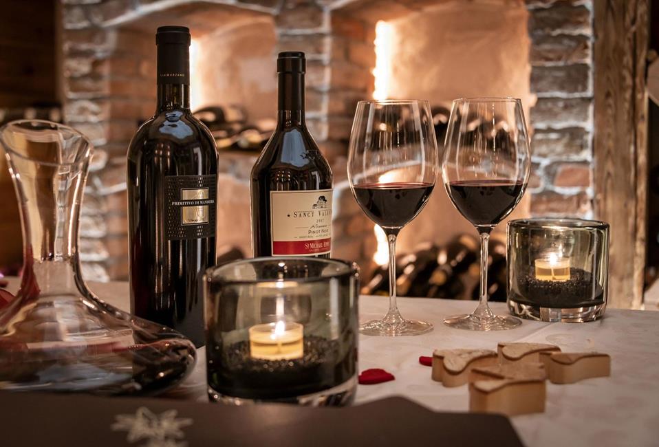 Two glasses of red wine, fine wine bottles, candlelight and wooden decor in a rustic wine cellar.
