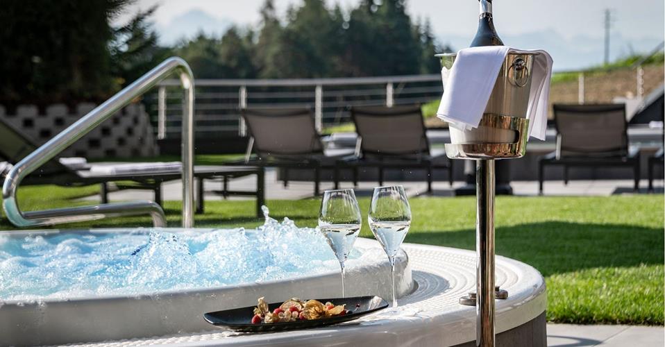 Outdoor whirlpool with bubbling water, two glasses of sparkling wine, fruit plate, and champagne cooler.