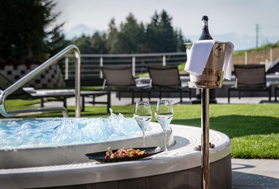 Outdoor whirlpool with bubbling water, two glasses of sparkling wine, fruit plate, and champagne cooler.