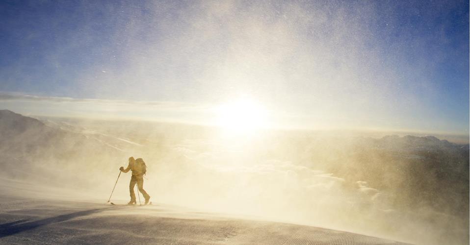 Scialpinista all’alba, avvolto dal vento e da una luce intensa.