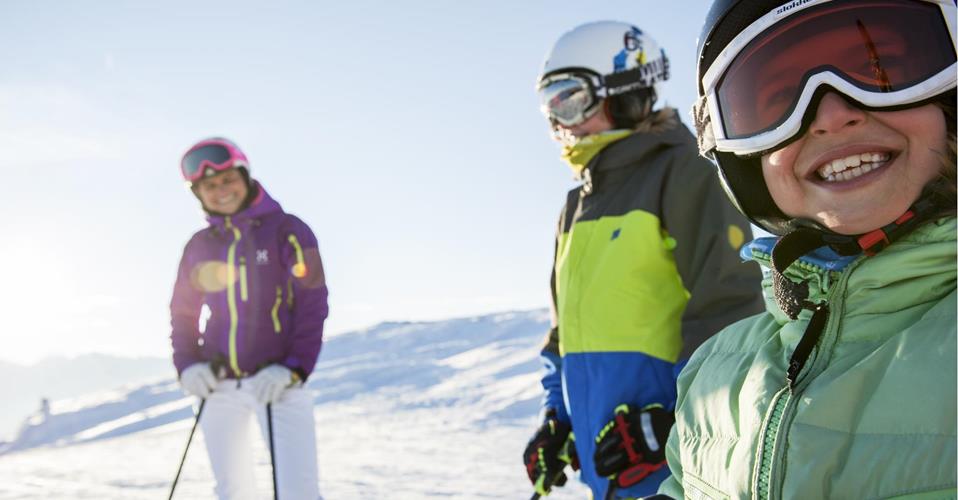 Tre bambini sorridenti in abbigliamento da sci si godono una giornata di sole sulle piste innevate.