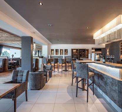 Our bar with elegant upholstered furniture, illuminated counter and cozy alpine-style booths.