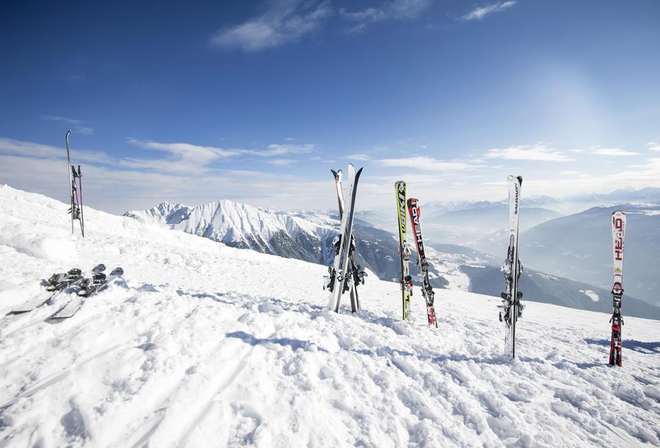 Sci piantati nella neve su una vetta con vista panoramica sulle Dolomiti innevate e cielo azzurro.