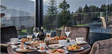 Ricca colazione con panini freschi, frutta, affettati e bevande calde con vista sulle montagne.