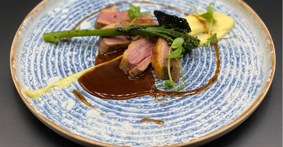 Fein angerichtetes Gourmetgericht mit rosa gebratenem Fleisch, Brokkolini, Kartoffelpüree und dunkler Jus