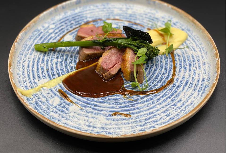 Piatto gourmet elegantemente impiattato con carne rosata, broccolini, purè di patate e salsa scura