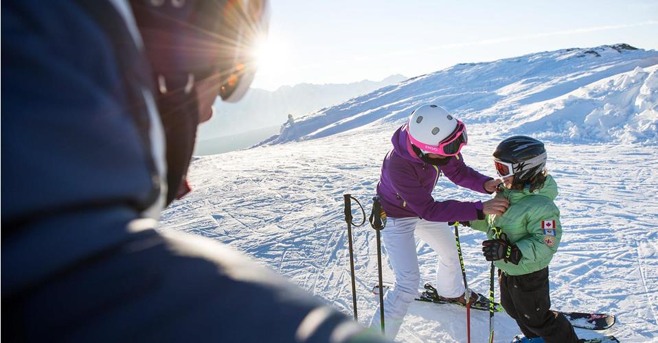 Ski instructor helps a child get dressed on a sunny, snowy ski slope.        ChatGPT fragen
